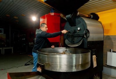 in a small roasting factory worker stands near the roasting machine monitoring the degree of roasting