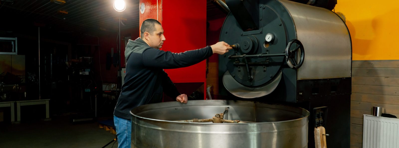 in a small roasting factory worker stands near the roasting machine monitoring the degree of roasting